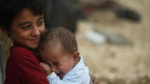 Refugee boy holds his sister outside the family tent